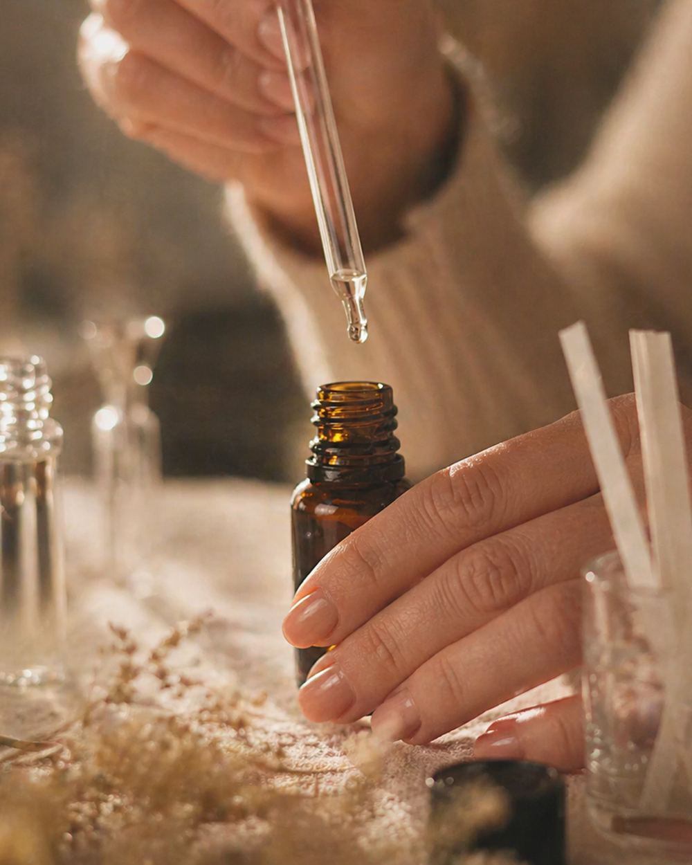 Dłonie odmierzające pipetą olejek zapachowy nad ciemną buteleczką w pracowni OLGY